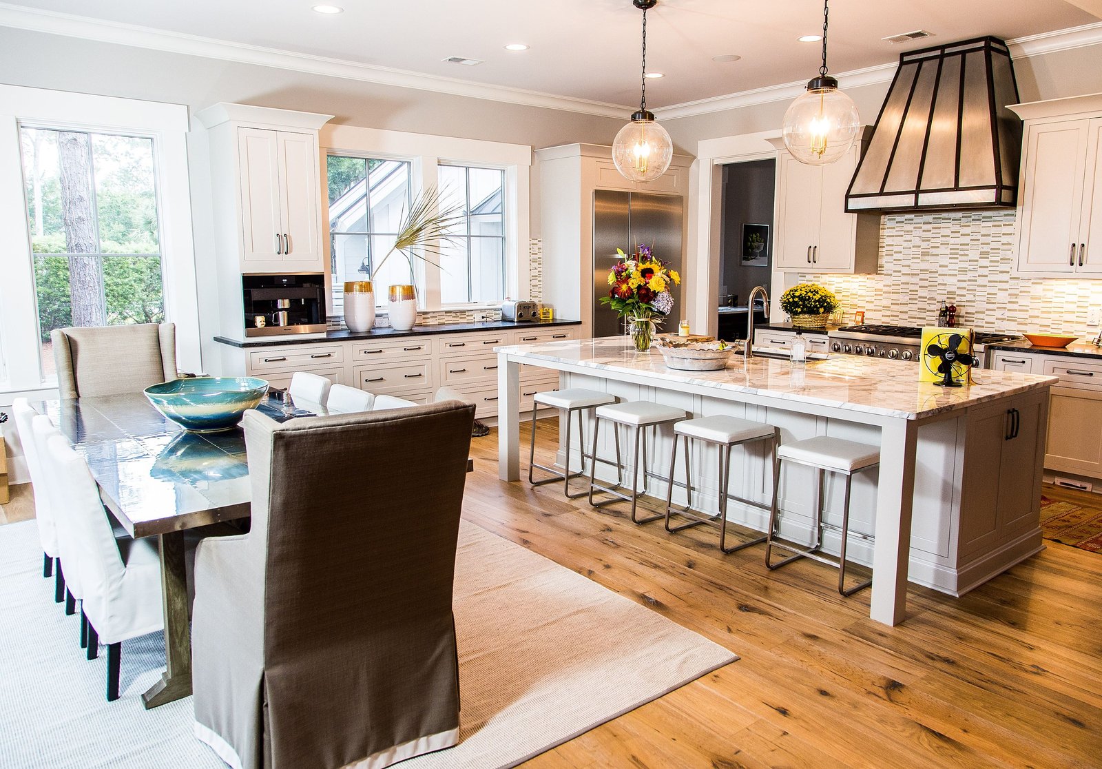 Bright island kitchen with a black range hood, pendant lights and a breakfast table