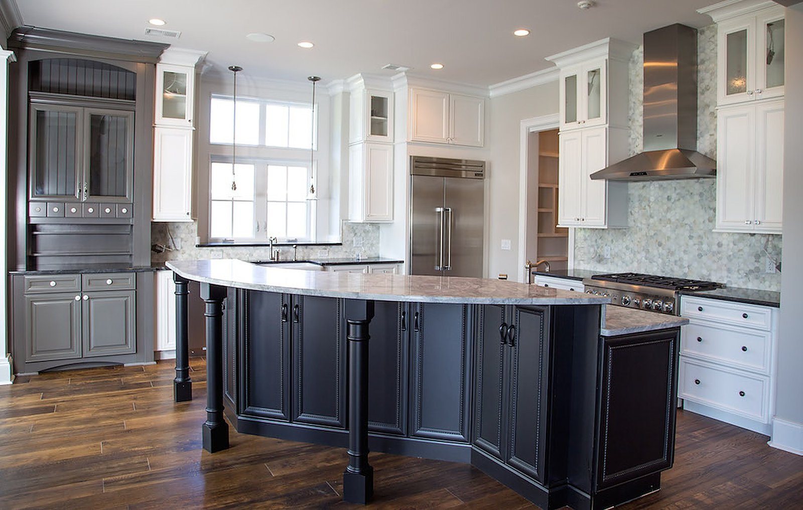 Kitchen with a dark island, white perimeter cabinets and a marble backsplash
